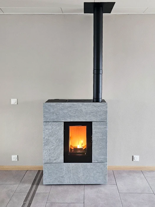 Flammes orange et jaunes s'élèvent d'un lit de granulés de bois cylindriques en combustion, avec arrière-plan de briques réfractaires