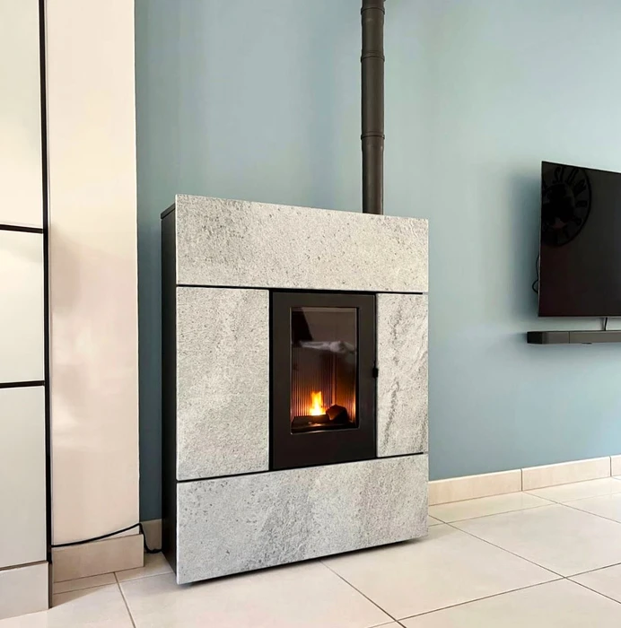 Intérieur chaleureux avec poêle à bois en fonte noire et porte vitrée, panier en osier contenant petit bois d'allumage, casier métallique rempli de bûches fendues